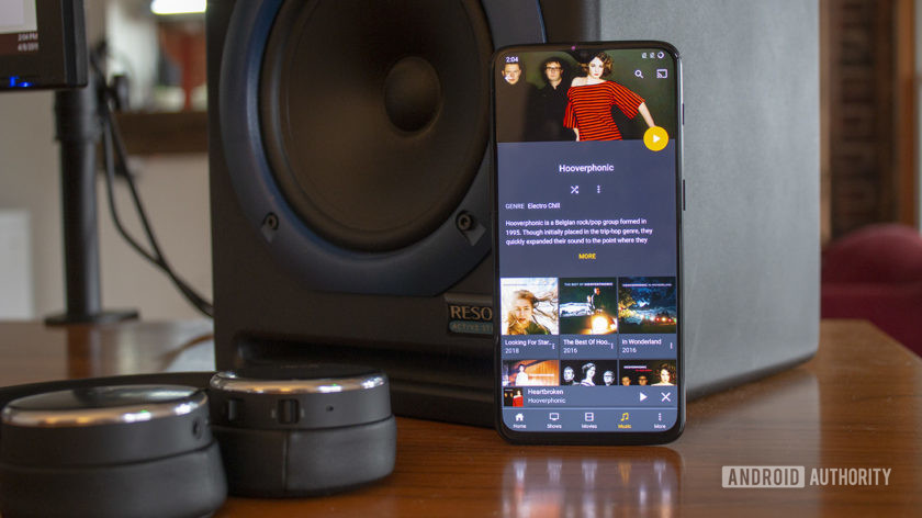 A smartphone leaning up against a speaker. The smartphone has the Plex music player on its display.